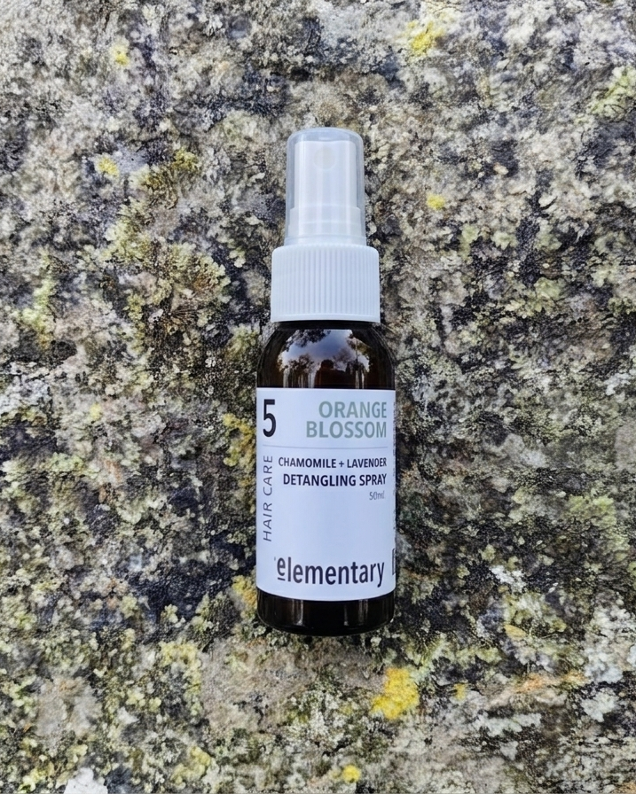 Bottle of 'Elementary' detangling spray on a textured stone surface